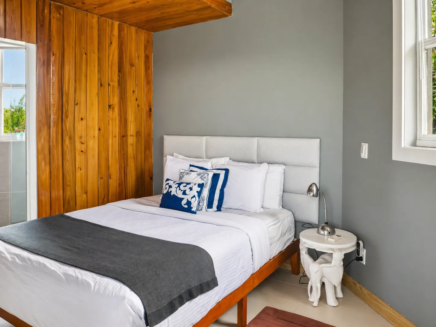 Pool House bedroom, queen bed with a wood-panelled wall and garden windows.